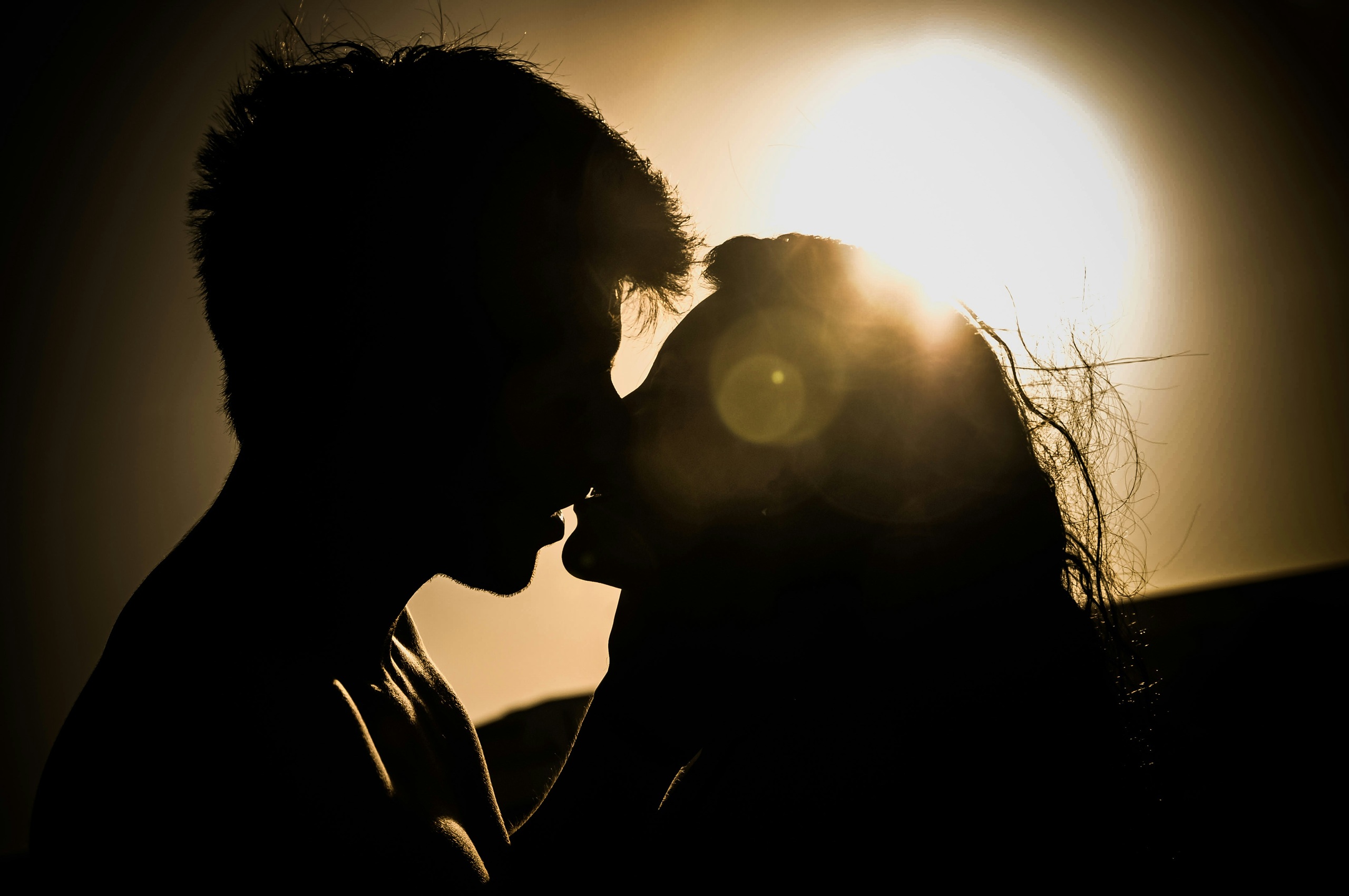 Casal em silhueta prestes a beijar-se com iluminação quente e sombras dramáticas ao fundo
