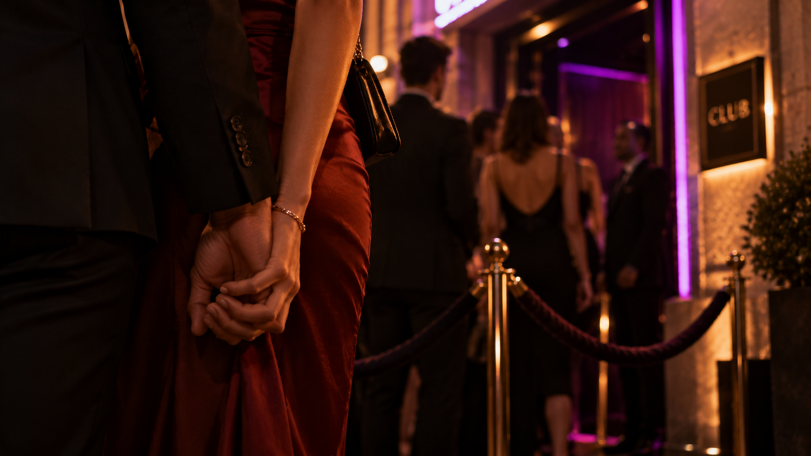 Mãos de casal entrelaçadas na fila de entrada de um clube noturno com luz roxa e outros casais ao fundo, ambiente elegante e discreto